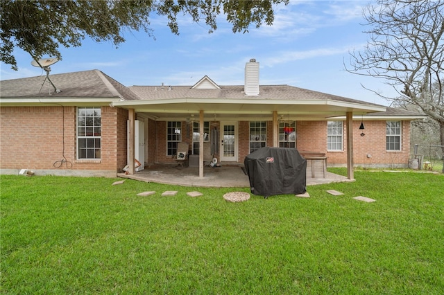 back of property with a patio area, a lawn, a chimney, and brick siding