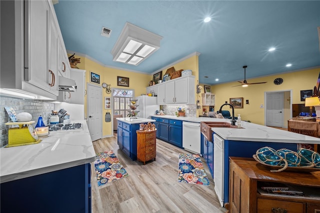 kitchen with blue cabinets, visible vents, light wood-type flooring, white appliances, and a peninsula