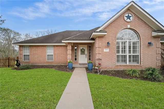 view of front of house with brick siding, a shingled roof, a front yard, and fence