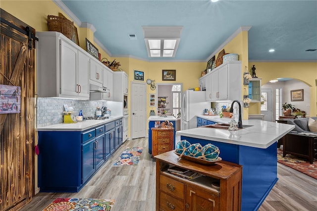 kitchen with freestanding refrigerator, arched walkways, white cabinets, blue cabinets, and a sink