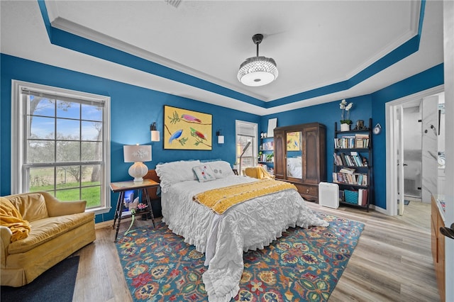 bedroom with a raised ceiling, wood finished floors, baseboards, and ornamental molding