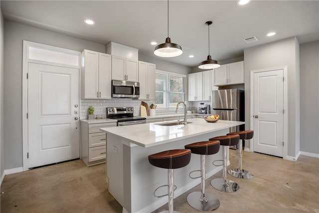 kitchen with pendant lighting, sink, stainless steel appliances, white cabinets, and a center island with sink