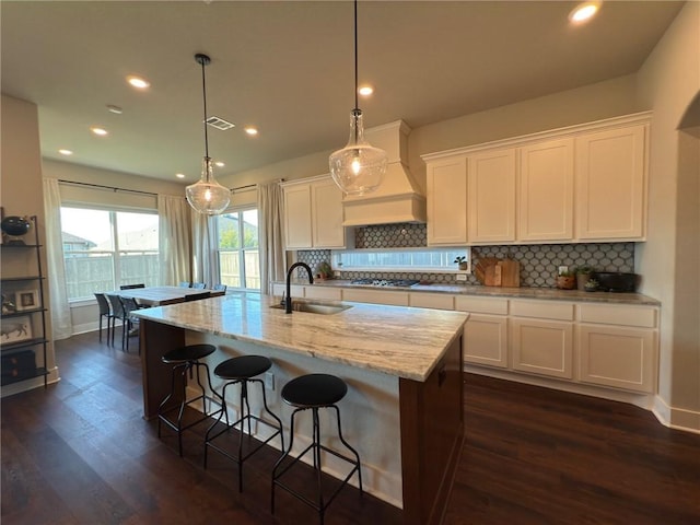 kitchen featuring sink, pendant lighting, a center island with sink, white cabinets, and custom exhaust hood