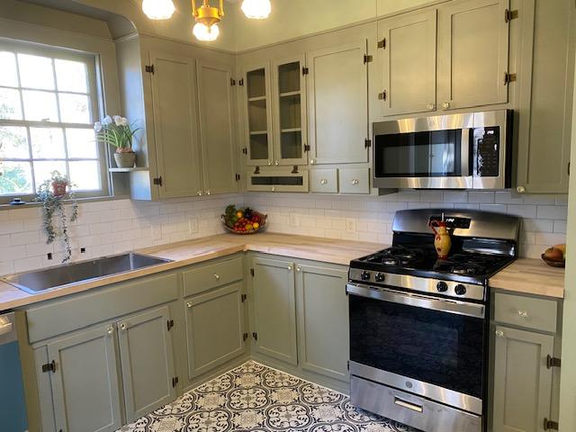 kitchen featuring appliances with stainless steel finishes, decorative backsplash, sink, a notable chandelier, and light tile patterned floors