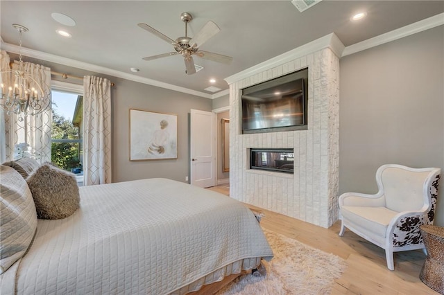 bedroom with light wood-type flooring, ceiling fan with notable chandelier, a large fireplace, and crown molding