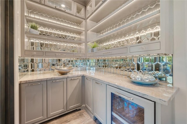 bar featuring gray cabinetry, decorative backsplash, light stone countertops, and beverage cooler