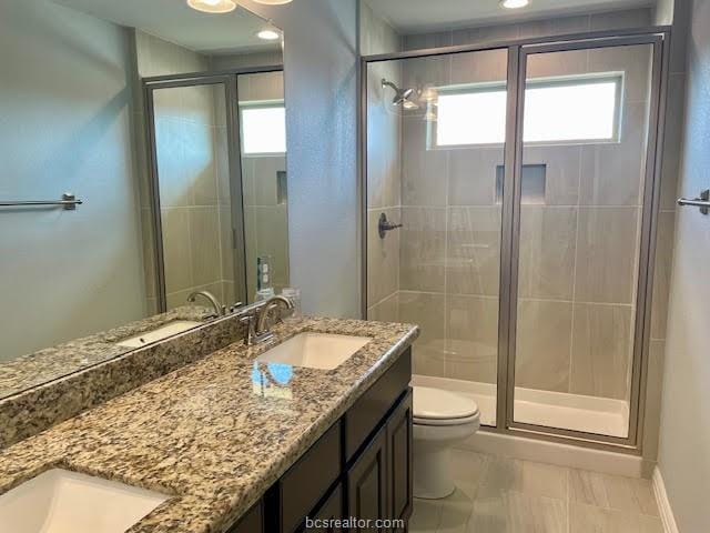 bathroom featuring toilet, a stall shower, double vanity, and a sink