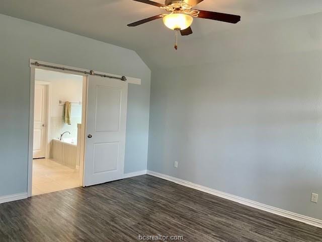 unfurnished bedroom featuring a barn door, baseboards, dark wood finished floors, ceiling fan, and vaulted ceiling