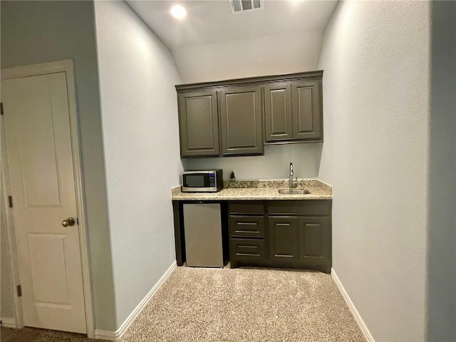 bar with refrigerator, visible vents, stainless steel microwave, light carpet, and a sink