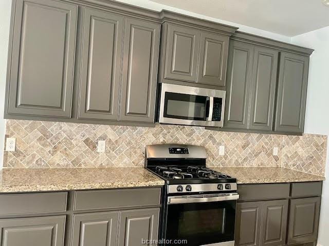 kitchen featuring stainless steel appliances, light stone counters, backsplash, and gray cabinetry