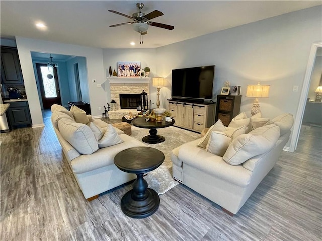 living area with recessed lighting, a ceiling fan, a stone fireplace, wood finished floors, and baseboards