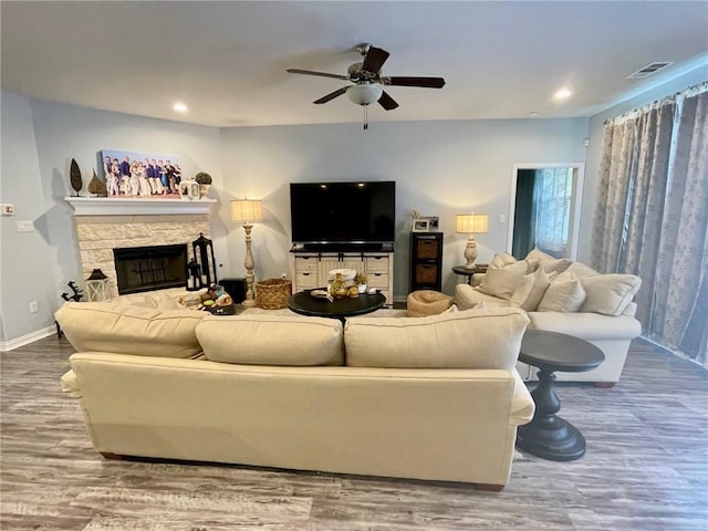 living room featuring recessed lighting, a ceiling fan, a stone fireplace, wood finished floors, and baseboards