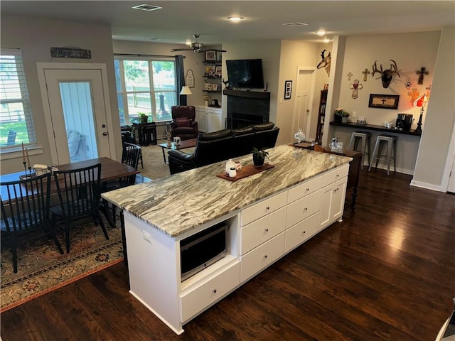 202 N Hearne St, Franklin, TX 77856 - kitchen featuring light stone countertops, stainless steel microwave, white cabinetry, dark wood-type flooring, and a fireplace