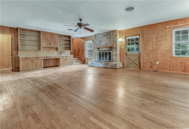 1500 Galde St, College Station, TX 77840 - unfurnished living room with wood walls, light wood-style flooring, ceiling fan, and a brick fireplace