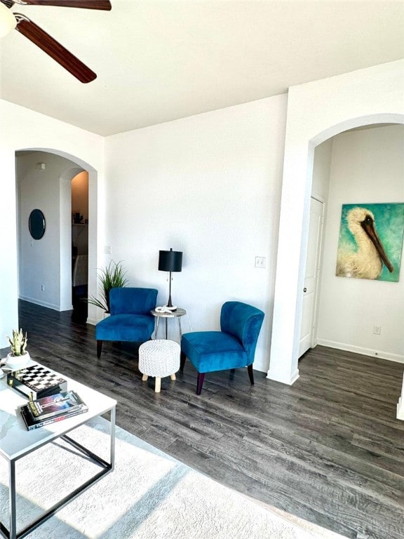 living area featuring dark wood-style floors, arched walkways, baseboards, and a ceiling fan