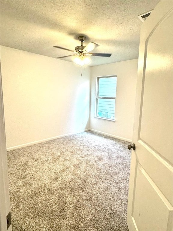 carpeted empty room with a ceiling fan, visible vents, baseboards, and a textured ceiling