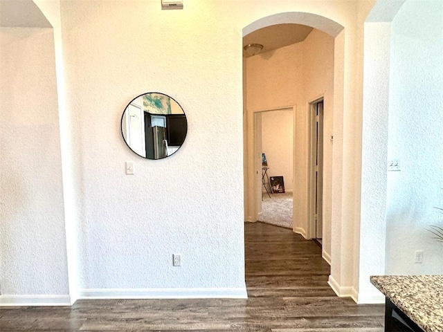 corridor featuring arched walkways, dark wood finished floors, and baseboards