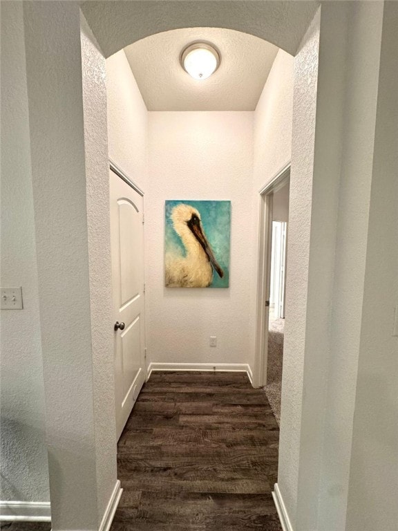 hall with dark wood-type flooring, arched walkways, a textured wall, and a textured ceiling