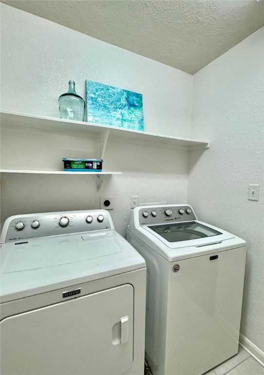 washroom featuring washing machine and clothes dryer, light tile patterned floors, a textured wall, a textured ceiling, and laundry area