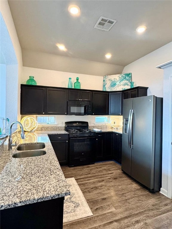 kitchen featuring visible vents, wood finished floors, light stone countertops, black appliances, and a sink