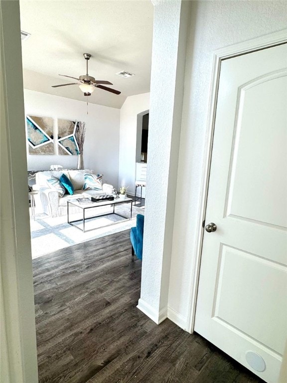 corridor featuring a textured wall, dark wood-type flooring, visible vents, and baseboards