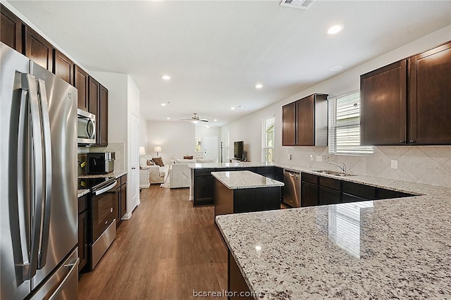 kitchen featuring a center island, dark wood-type flooring, stainless steel appliances, light stone counters, and kitchen peninsula