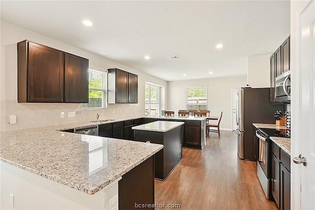 kitchen with kitchen peninsula, stainless steel appliances, a kitchen island, and light stone counters