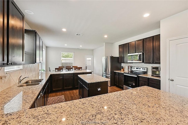 kitchen featuring light stone countertops, a kitchen island, dark hardwood / wood-style flooring, kitchen peninsula, and stainless steel appliances