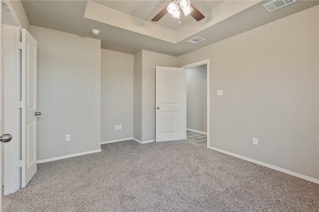 spare room featuring ceiling fan, light colored carpet, and a tray ceiling