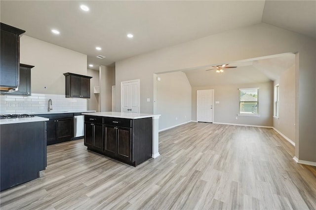 kitchen with lofted ceiling, decorative backsplash, a center island, stainless steel dishwasher, and light hardwood / wood-style floors