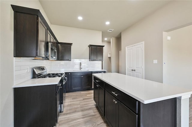 kitchen with a kitchen island, appliances with stainless steel finishes, tasteful backsplash, sink, and light hardwood / wood-style flooring