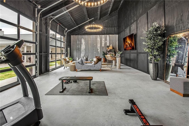 exercise room featuring wooden walls, high vaulted ceiling, a notable chandelier, and a healthy amount of sunlight