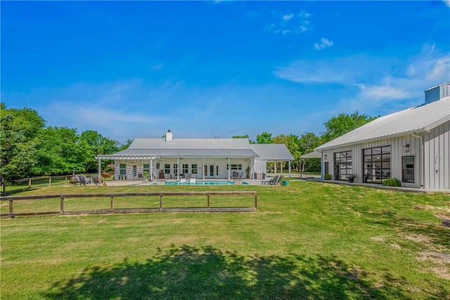 back of house with board and batten siding, a yard, metal roof, and an outdoor pool