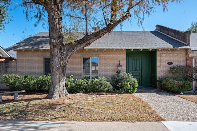 ranch-style home featuring brick siding, a chimney, and roof with shingles