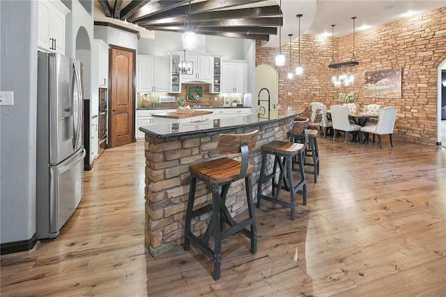 kitchen featuring decorative light fixtures, a center island with sink, white cabinetry, appliances with stainless steel finishes, and a kitchen breakfast bar