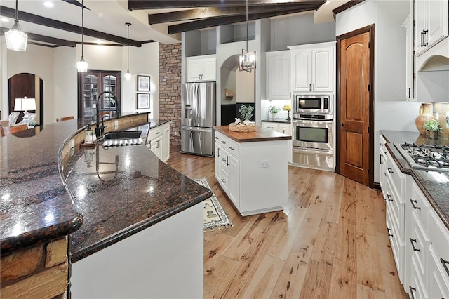 kitchen with pendant lighting, stainless steel appliances, a kitchen island with sink, and beamed ceiling