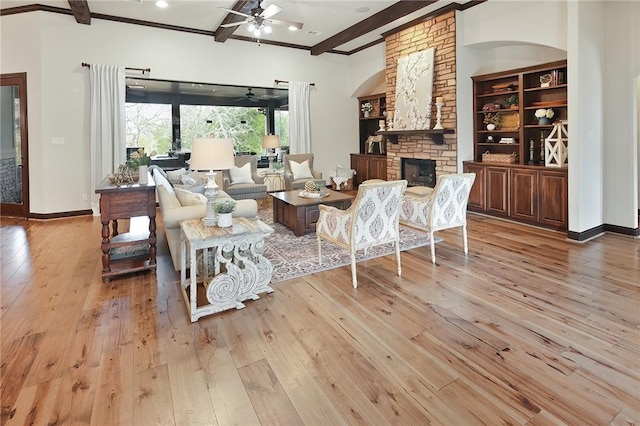 living room featuring ceiling fan, light hardwood / wood-style flooring, beam ceiling, and a stone fireplace