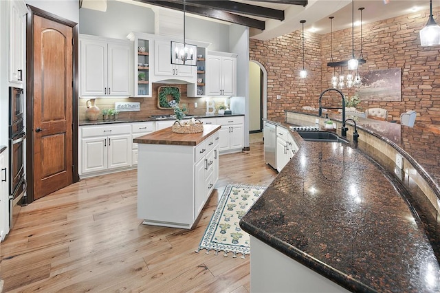 kitchen with decorative light fixtures, white cabinetry, a kitchen island with sink, and beamed ceiling