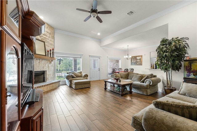 living area featuring crown molding, a fireplace, visible vents, wood finished floors, and ceiling fan with notable chandelier