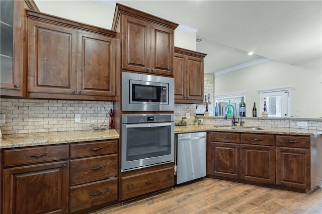 kitchen featuring a sink, stainless steel appliances, crown molding, light wood-style floors, and backsplash