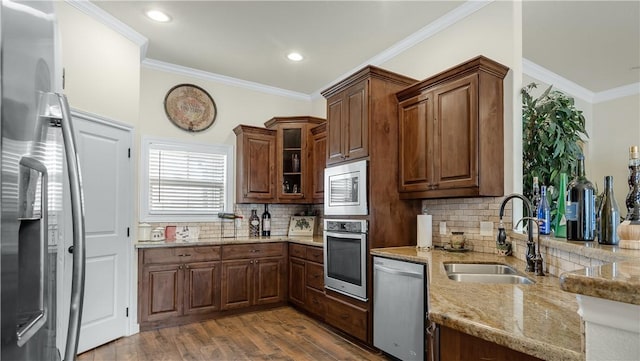 kitchen with light stone counters, crown molding, appliances with stainless steel finishes, glass insert cabinets, and a sink