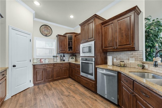 kitchen featuring stainless steel appliances, a sink, wood finished floors, ornamental molding, and glass insert cabinets