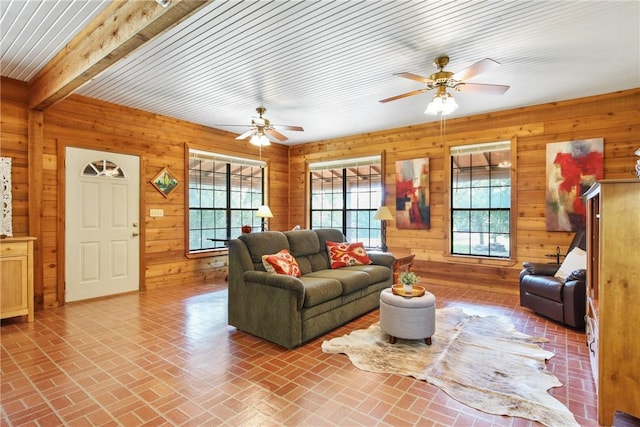 living room featuring wood walls, ceiling fan, and beam ceiling