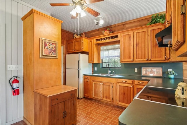 kitchen featuring ceiling fan, sink, white fridge, and wood walls