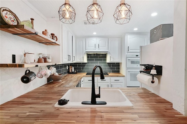 kitchen featuring double oven, butcher block counters, white cabinets, and pendant lighting