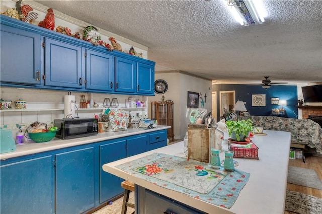 kitchen featuring ceiling fan, blue cabinets, a textured ceiling, and light hardwood / wood-style flooring