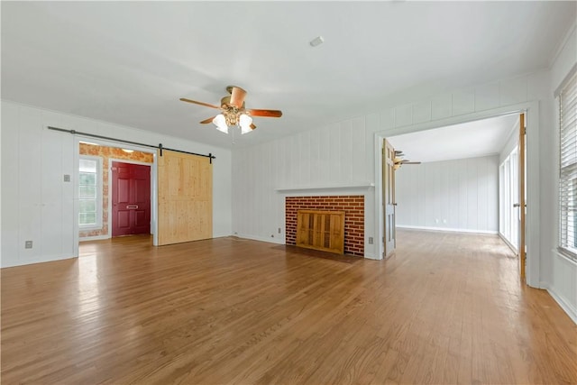 107 E N Ave, Bryan, TX 77801 - unfurnished living room with ceiling fan, a barn door, light wood-style flooring, a decorative wall, and baseboards