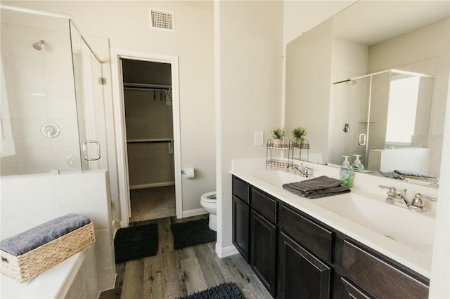 full bath featuring wood finished floors, visible vents, a stall shower, a sink, and a walk in closet