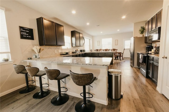 kitchen with light wood-type flooring, black electric range oven, backsplash, a peninsula, and dark brown cabinets