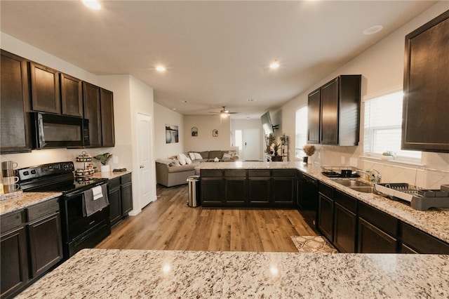 kitchen featuring light stone counters, light wood finished floors, a sink, black appliances, and open floor plan